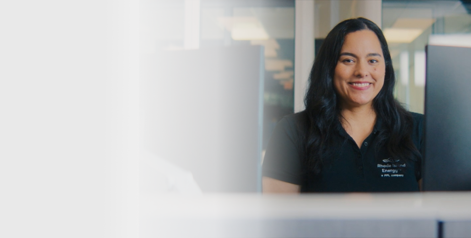 Woman with dark hair wearing a dark blue polo shirt and smiling, sitting between two computer monitors